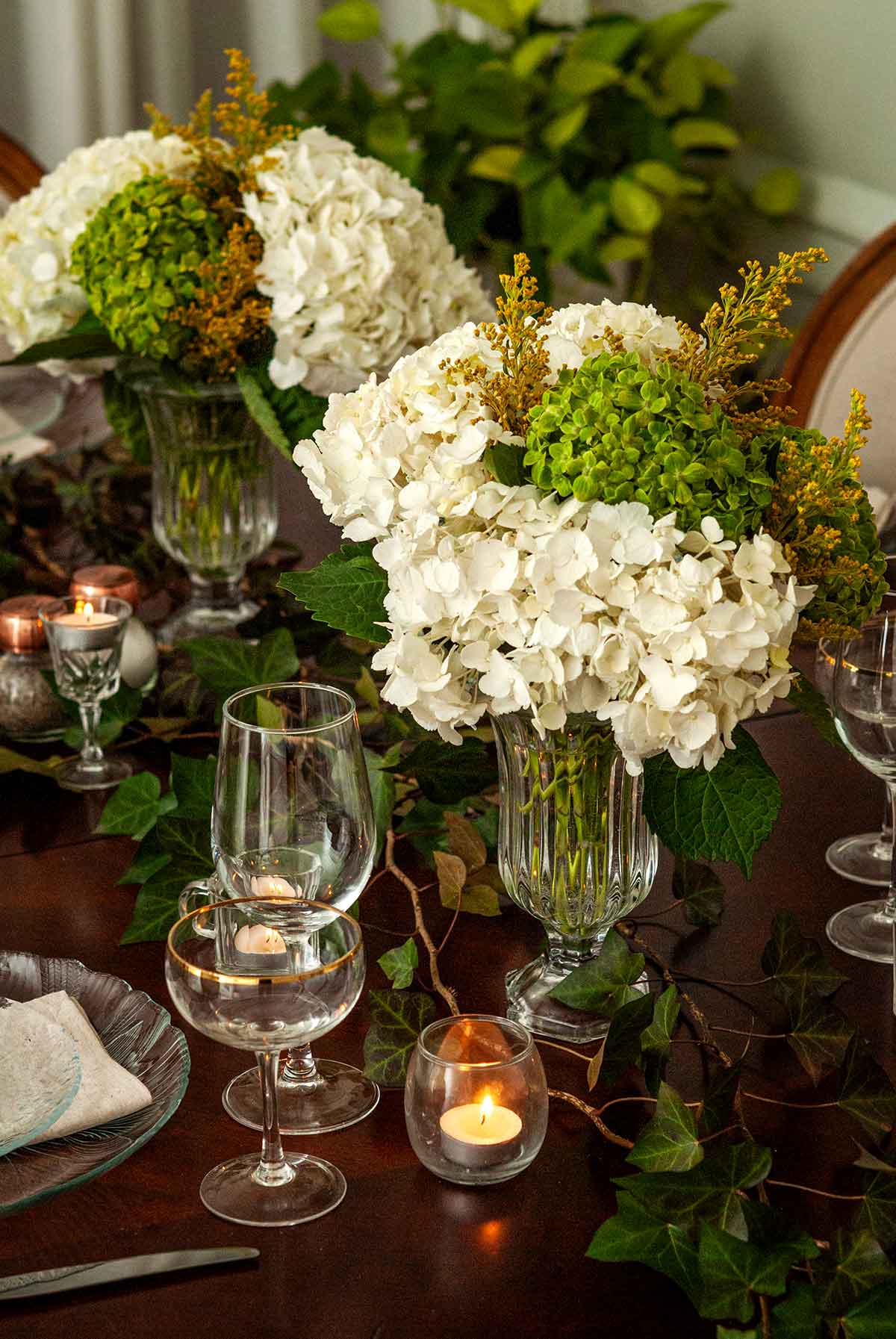 A table elegantly decorated with ivy, flowers, glassware and candles.