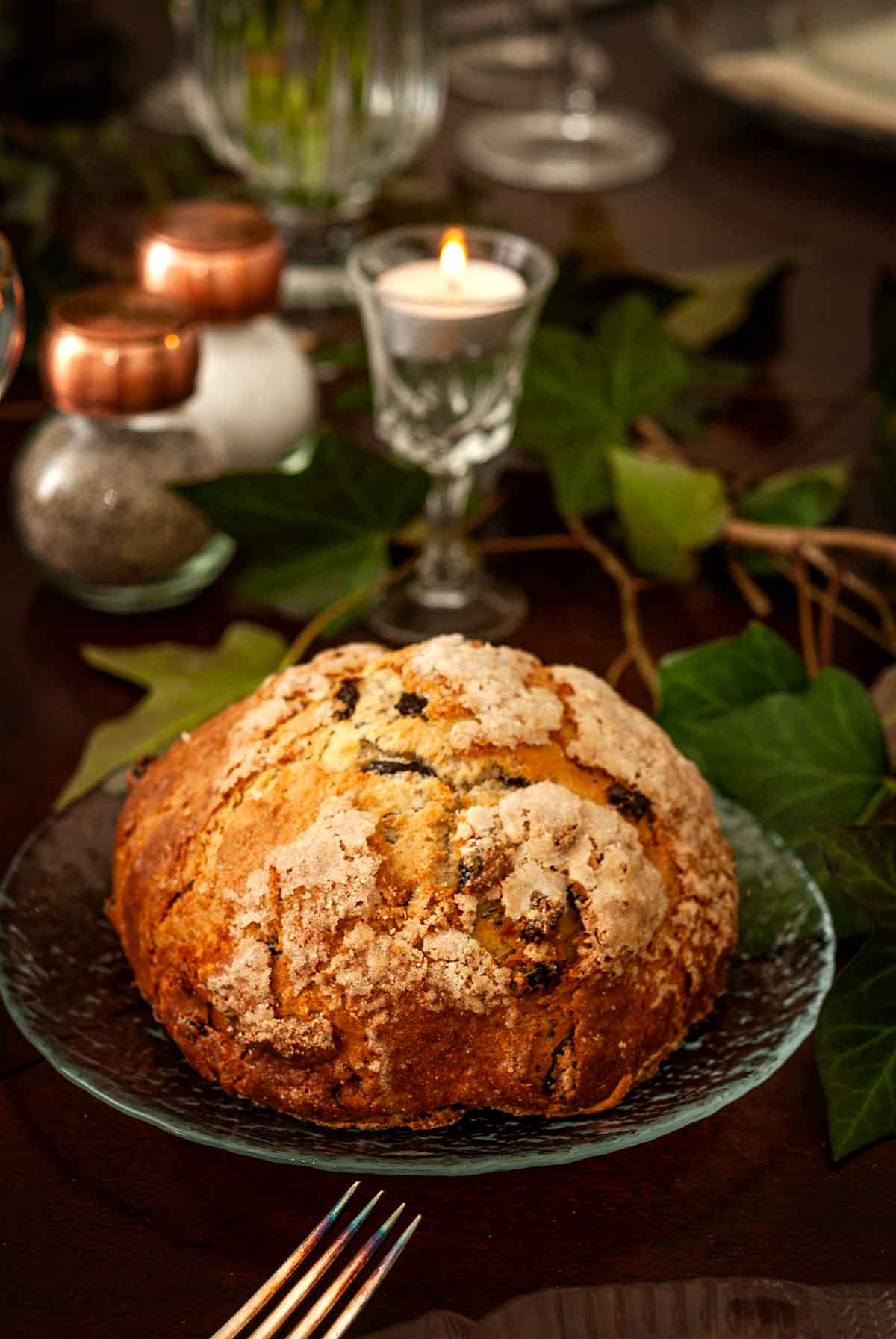 A plate with soda bread on a table with ivy, candles and salt and pepper shakers.