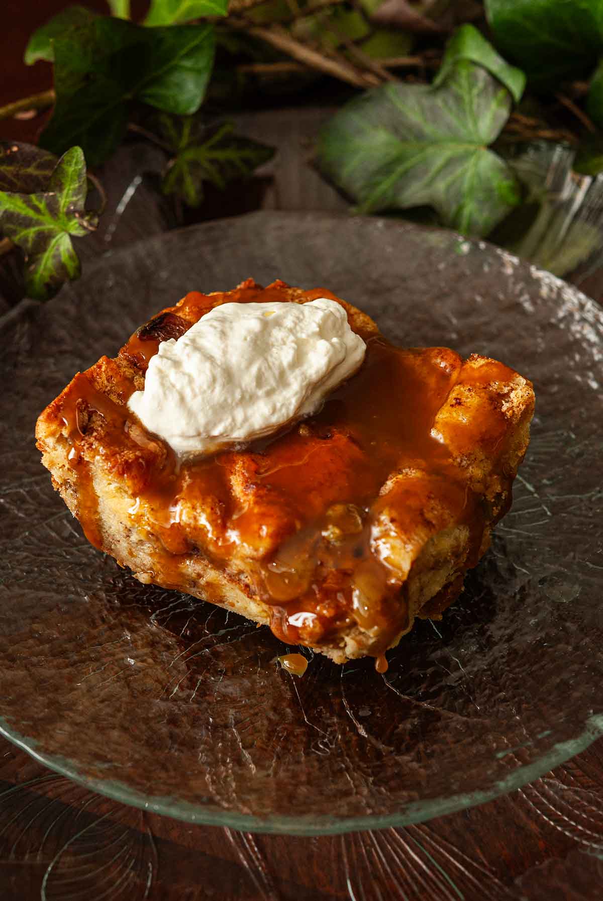 A slice of salted caramel pudding on a plate, topped with cream, surrounded by ivy.