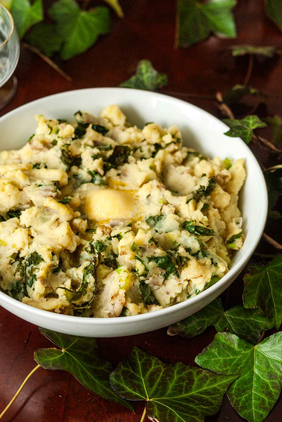 A bowl of colcannon on a table with butter in the center, surrounded by ivy.