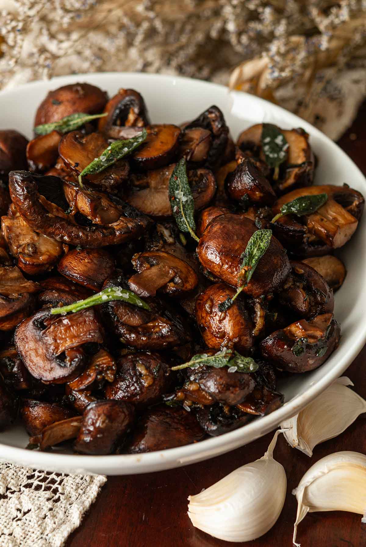 A bowl of sage and garlic butter in a bowl beside 3 cloves of garlic.