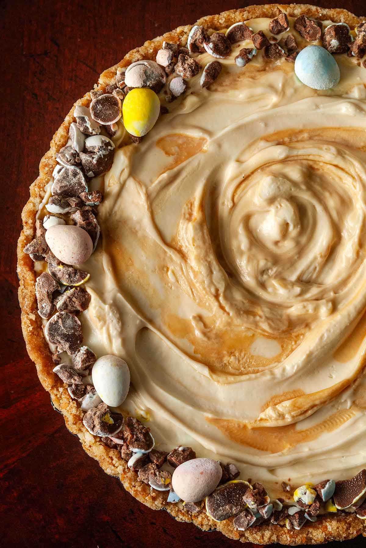 A cheesecake, swirled with caramel, and garnished with little chocolate eggs around the edges.