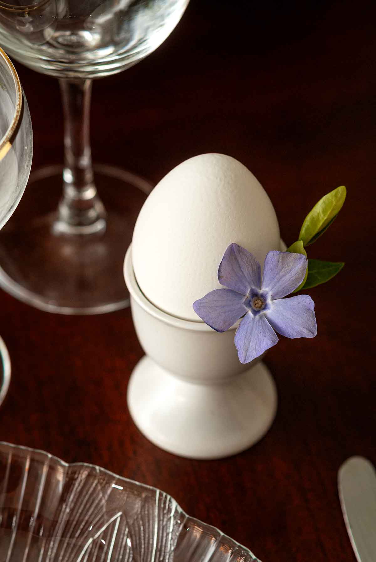 An egg in an egg cup with a flower tucked in the cup.