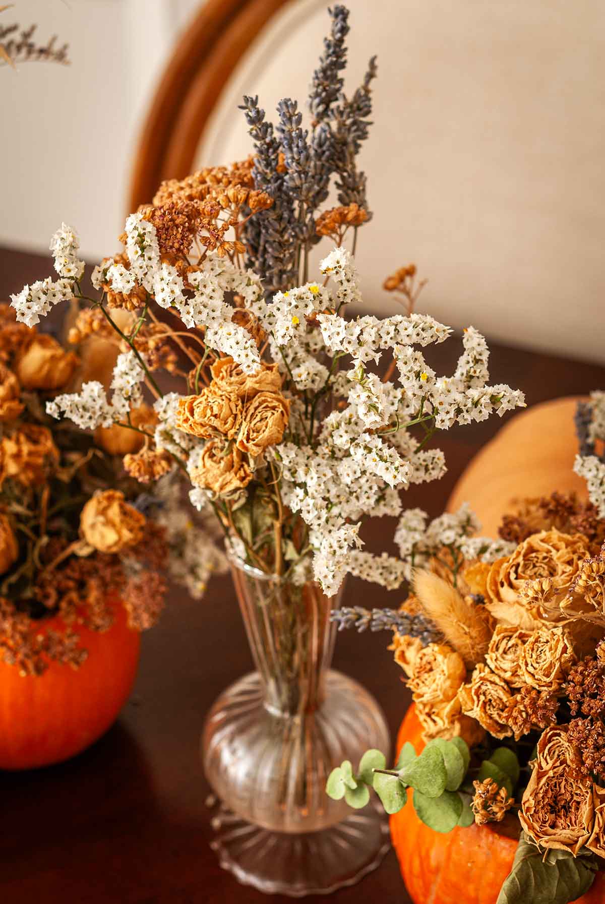 A glass vase of dry flowers next to pumpkins.