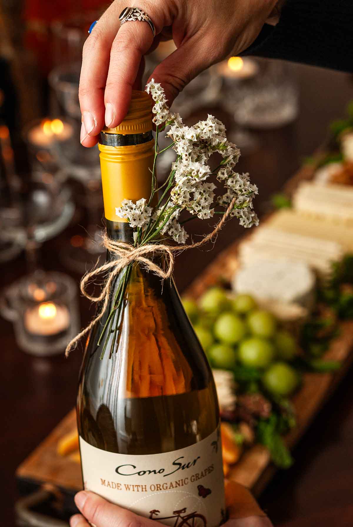 A hand talking the top off of a wine bottle tied with flowers.