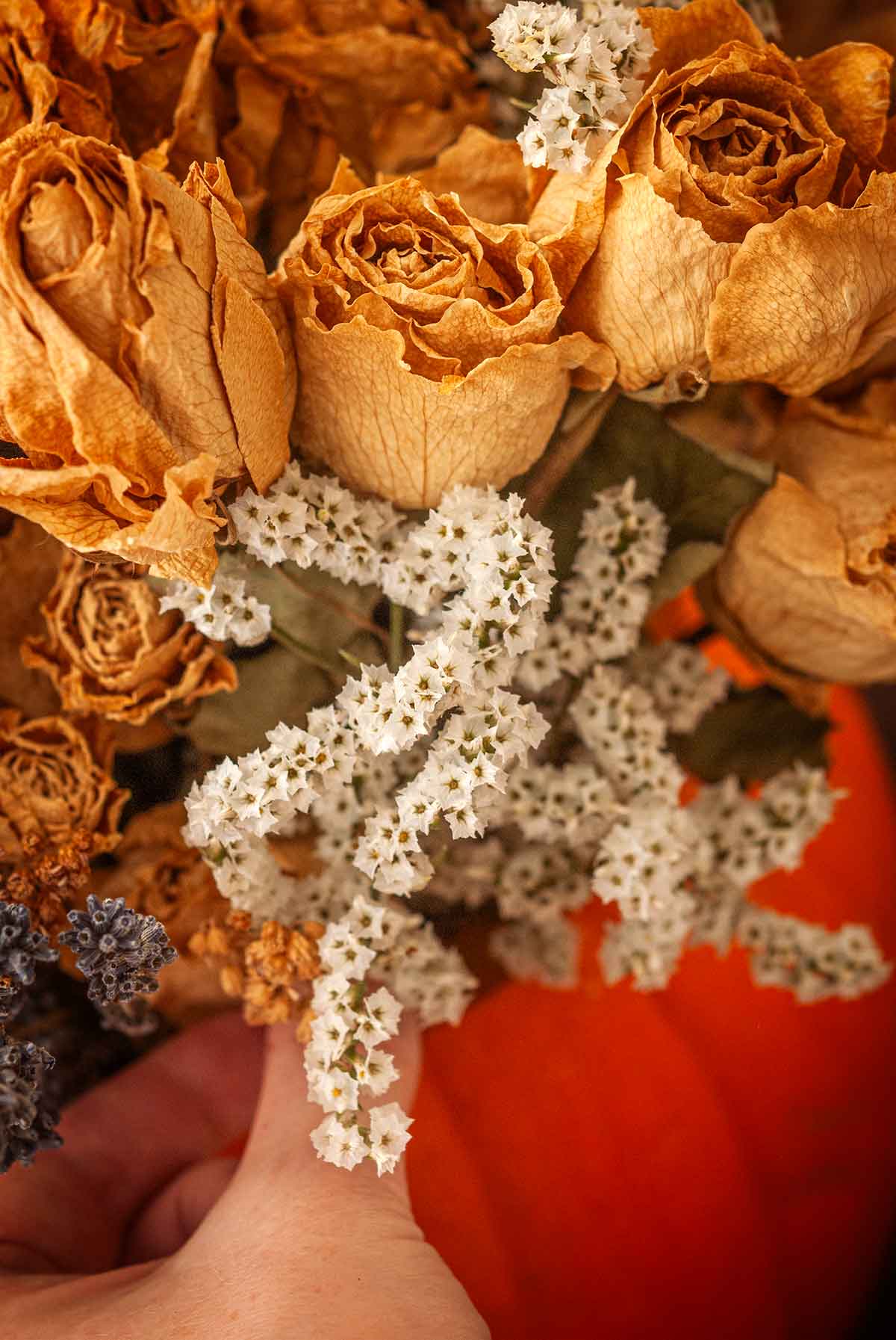 Fingers placing dry statice in a pumpkin with other flowers.