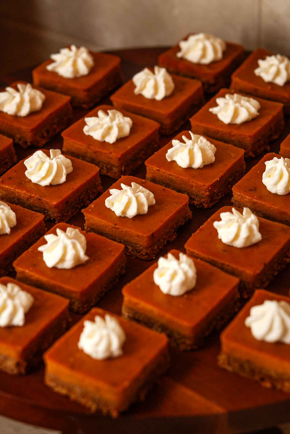 Mini pumpkin pie squares topped with chipped cream on a board.