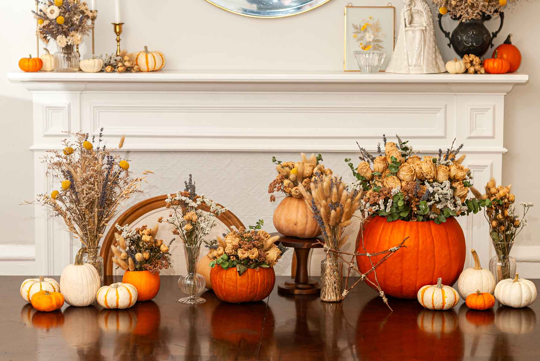 A row of pumpkins and pumpkin vases on a table in front of mantle decorated with pumpkins.