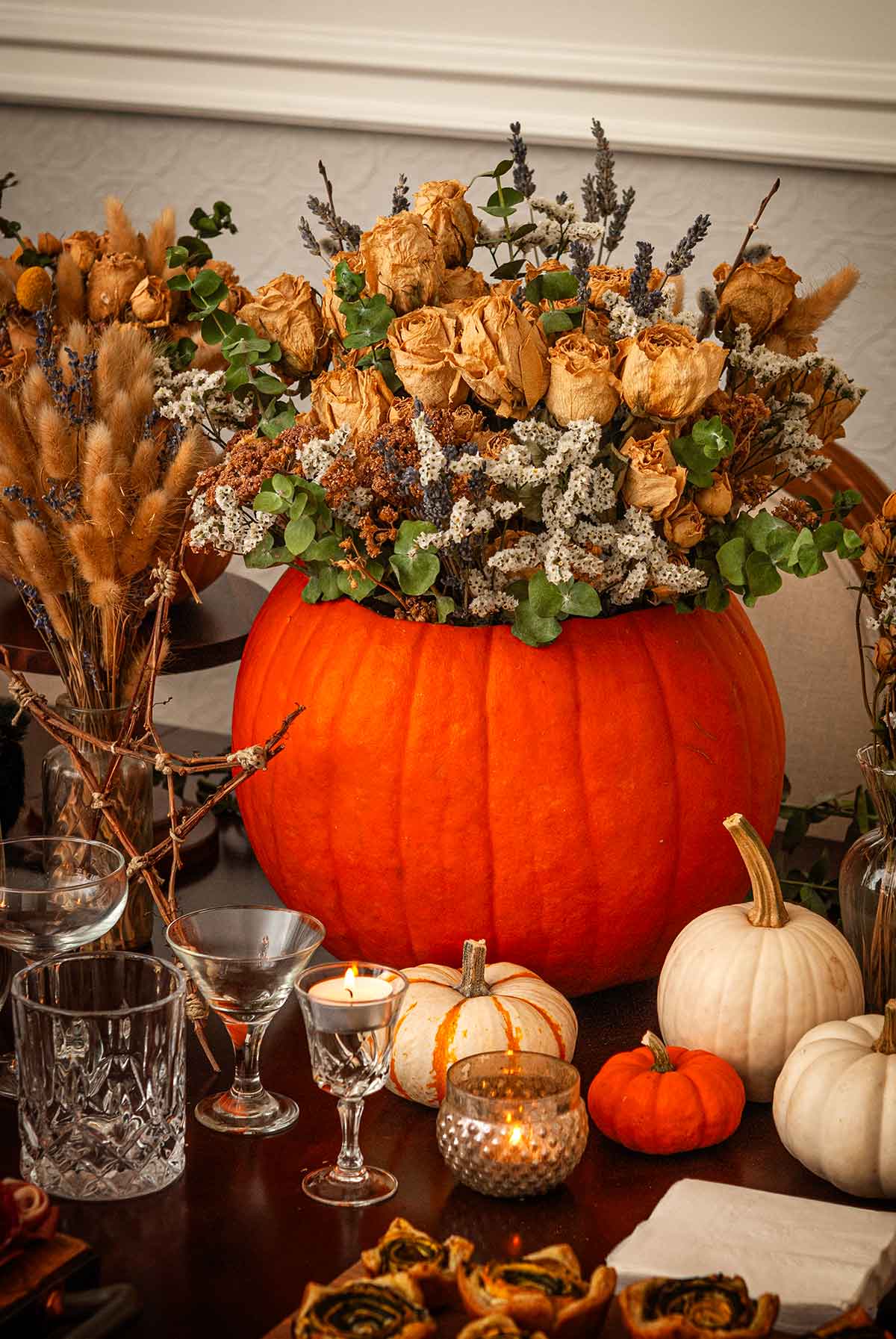 A large pumpkin bouquet surrounded by smaller pumpkins and glassware.