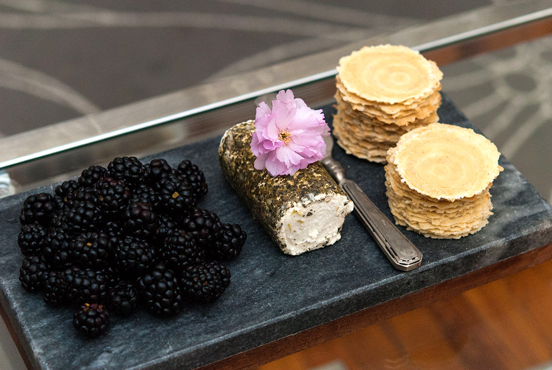 A cheese plate with blackberries, goat cheese and crackers on a dark slate