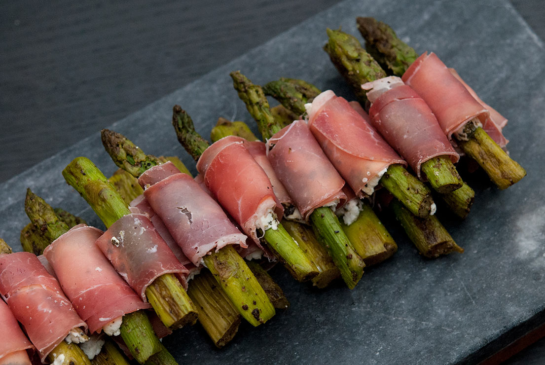 A pile of prosciutto-wrapped asparagus in a row on a marble plate.